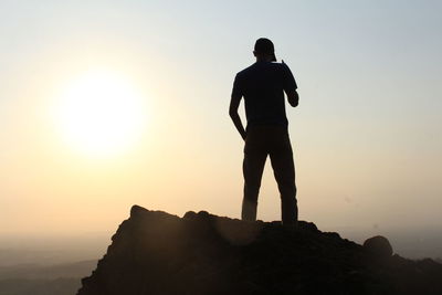 Rear view of silhouette man standing on rock against sky during sunset