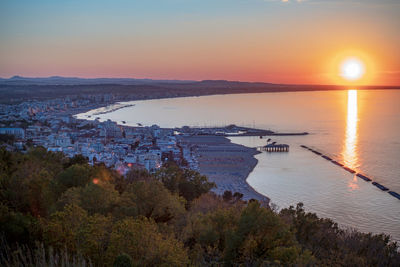 High angle view of sea and cityscape against sky at sunset