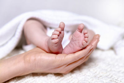 Close-up of mother hand touching baby feet lying on bed