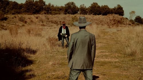 Rear view of man standing in front of cowboy on field