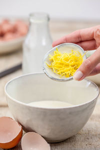 Cropped hand of person pouring ingredient in bowl on table