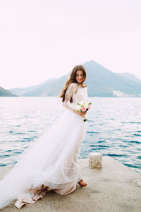 Woman standing on wall by sea against sky