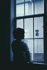 Rear view of boy looking through window at home