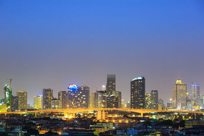 Illuminated buildings in city against clear sky at night