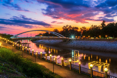 Illuminated bridge over river against sky at sunset