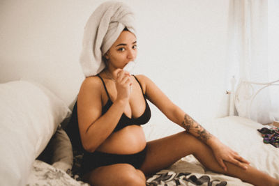 Portrait of pregnant woman in bikini sitting on bed at home