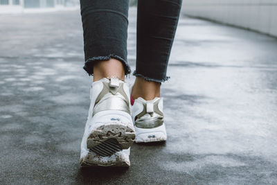 Low section of person wearing white shoe walking on road