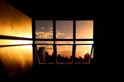 Silhouette building against sky during sunset seen through window