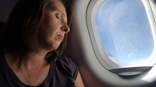 Close-up of young woman looking through airplane window