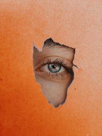 Close-up eye peeking through torn orange paper