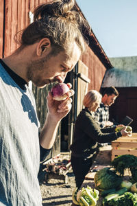 Mid adult male farmer smelling turnip with friends in background at market