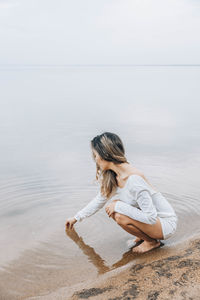 Rear view of woman sitting on beach against sky