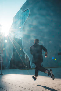 Rear view of man running on ball in city against sky