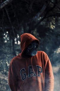 Midsection of person wearing mask standing against tree