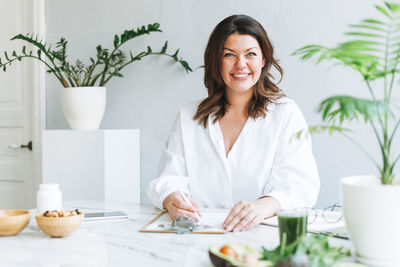 Young smiling brunette woman doctor nutritionist plus size in white shirt working at laptop 