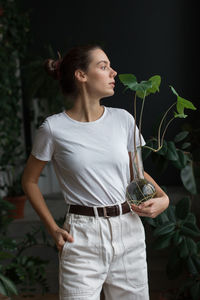 Young woman looking away while standing against plants