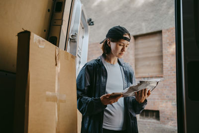 Female delivery person examining parcel while standing near van