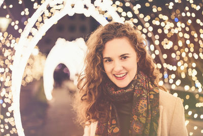 Beautiful curly hair smiling young woman in a coat outdoors with christmas lights and decoration