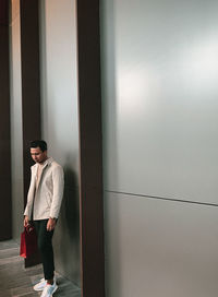 Young man looking away while standing against wall