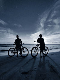 Silhouette people riding bicycles on beach against sky