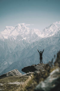 Rear view of man with arms raised standing against snowcapped mountain