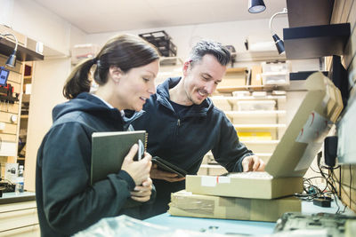 Smiling computer technicians looking in cardboard box at workshop