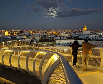 People in illuminated building against sky in city