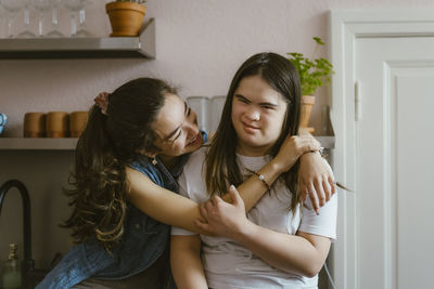 Happy young woman hugging sister with down syndrome in kitchen at home