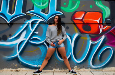 Full length of woman standing against graffiti wall