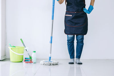 Low section of person with mop standing by cleaning equipment on tiled floor