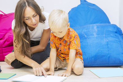 Mid adult teacher teaching student while sitting on floor against bean bag at school