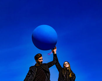 Portrait of young woman with balloons against blue sky
