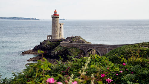 Lighthouse on sea by building against sky