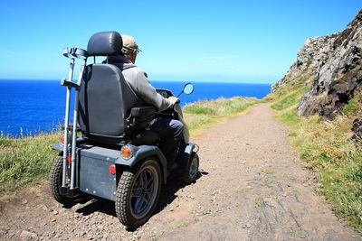 Rear view of man sitting on vehicle by sea during sunny day