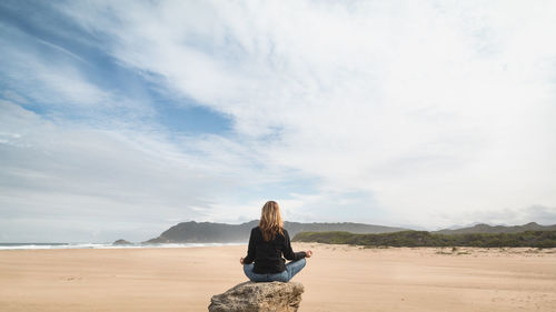 Rear view of woman meditating on beach