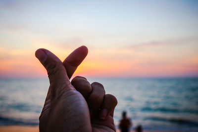 Close-up of hand against sea during sunset