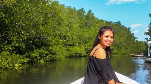Portrait of smiling young woman sitting in boat against trees