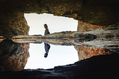 Man standing on rock by sea against sky