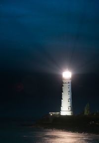 Illuminated lighthouse by sea against sky at night