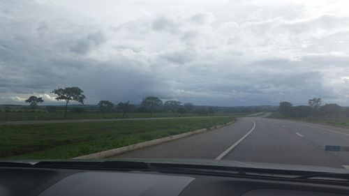 Road passing through field against cloudy sky