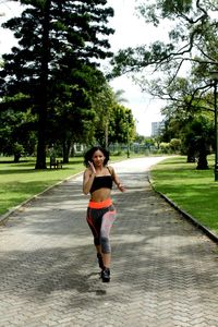Portrait of young woman running on footpath in park