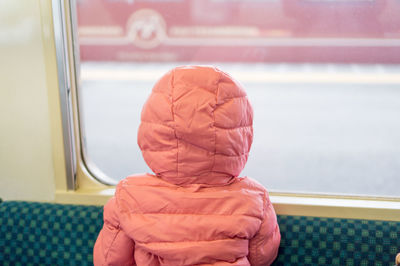 Rear view of child wearing hood by window in train