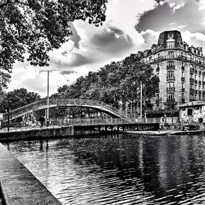 Bridge over river by buildings against sky