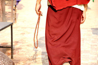 Rear view midsection of monk holding prayer beads while walking outdoors