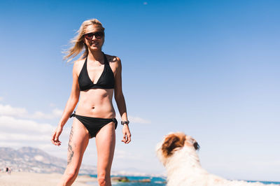 Woman in bikini with dog at beach against blue sky