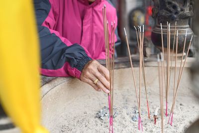 Midsection of person inserting incense stick in ash at temple
