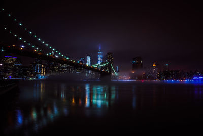 Illuminated buildings by river against sky at night