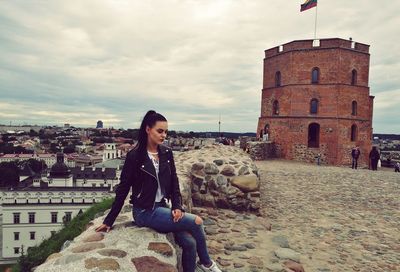 Young woman sitting on retaining wall at gediminas tower