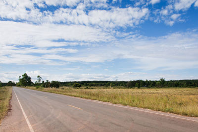 Empty road amidst field against sky