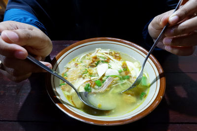 Midsection of person holding ice cream in bowl on table